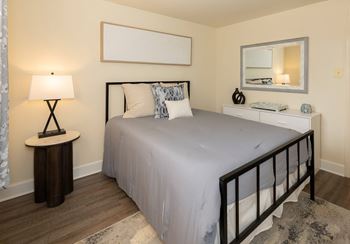 A bedroom with a bed, nightstand, and lamp at Hyde Park Apartments*, Essex, MD 21221